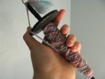 Teal, pink, and green spun yarn on black drop spindle held up in hand thumbnail.
