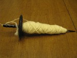 Undyed spun yarn on black drop spindle thumbnail.